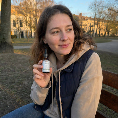 Жена държи бутилка CBD масло от Люцерн на открито в парк